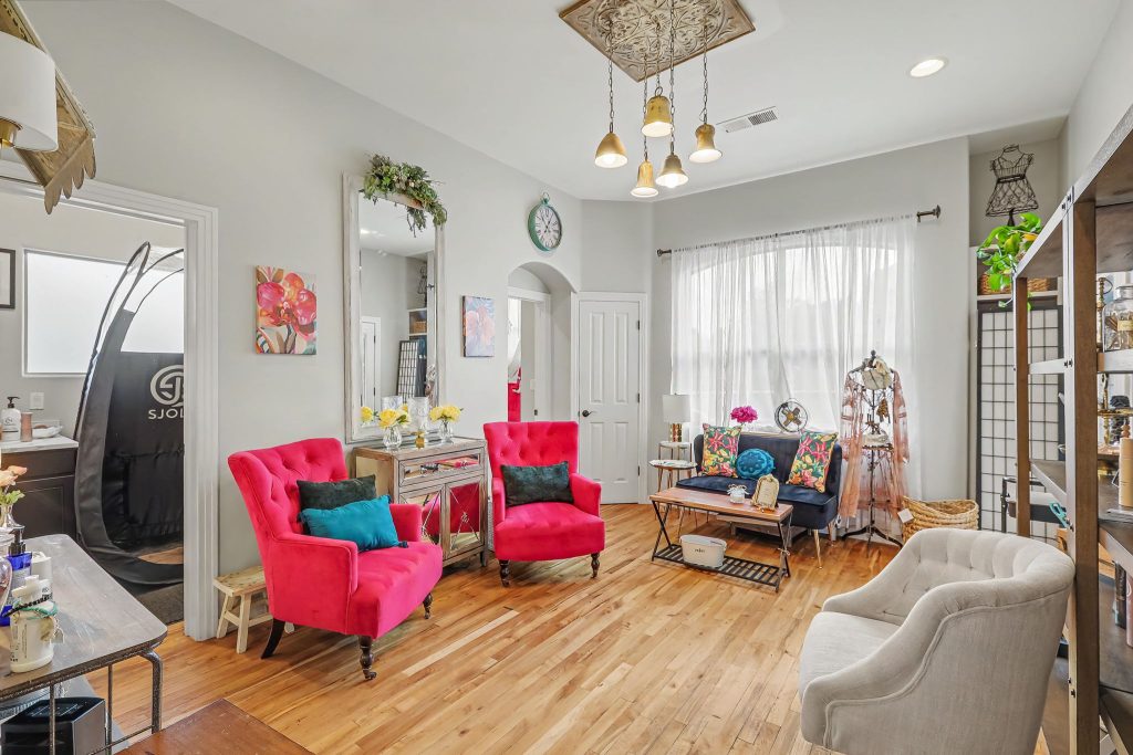 Living room with bright pink tufted chairs, colorful cushions, and a glass coffee table in a light-gray room.